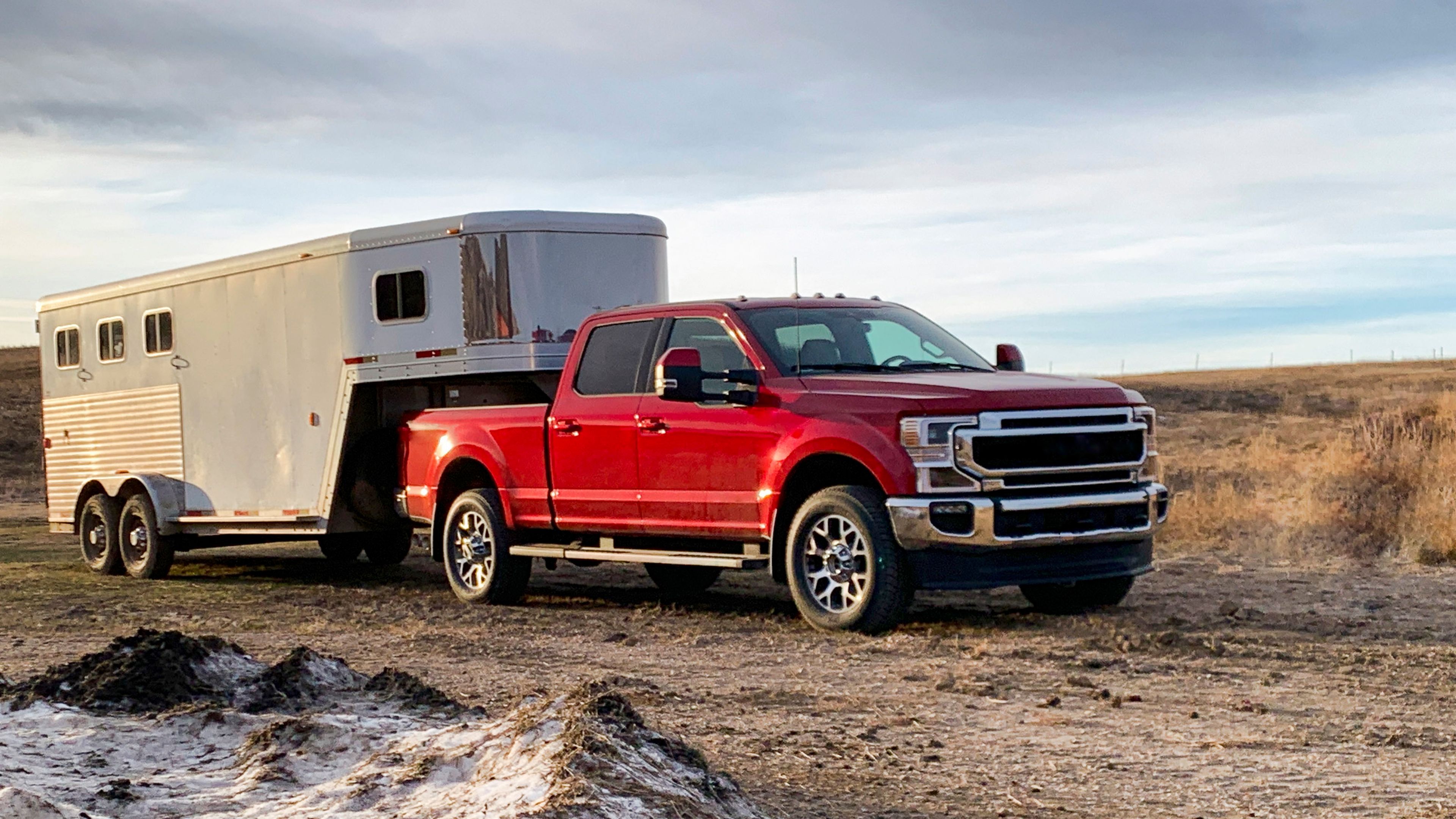 Red pickup truck towing a work trailer through a muddy rural road