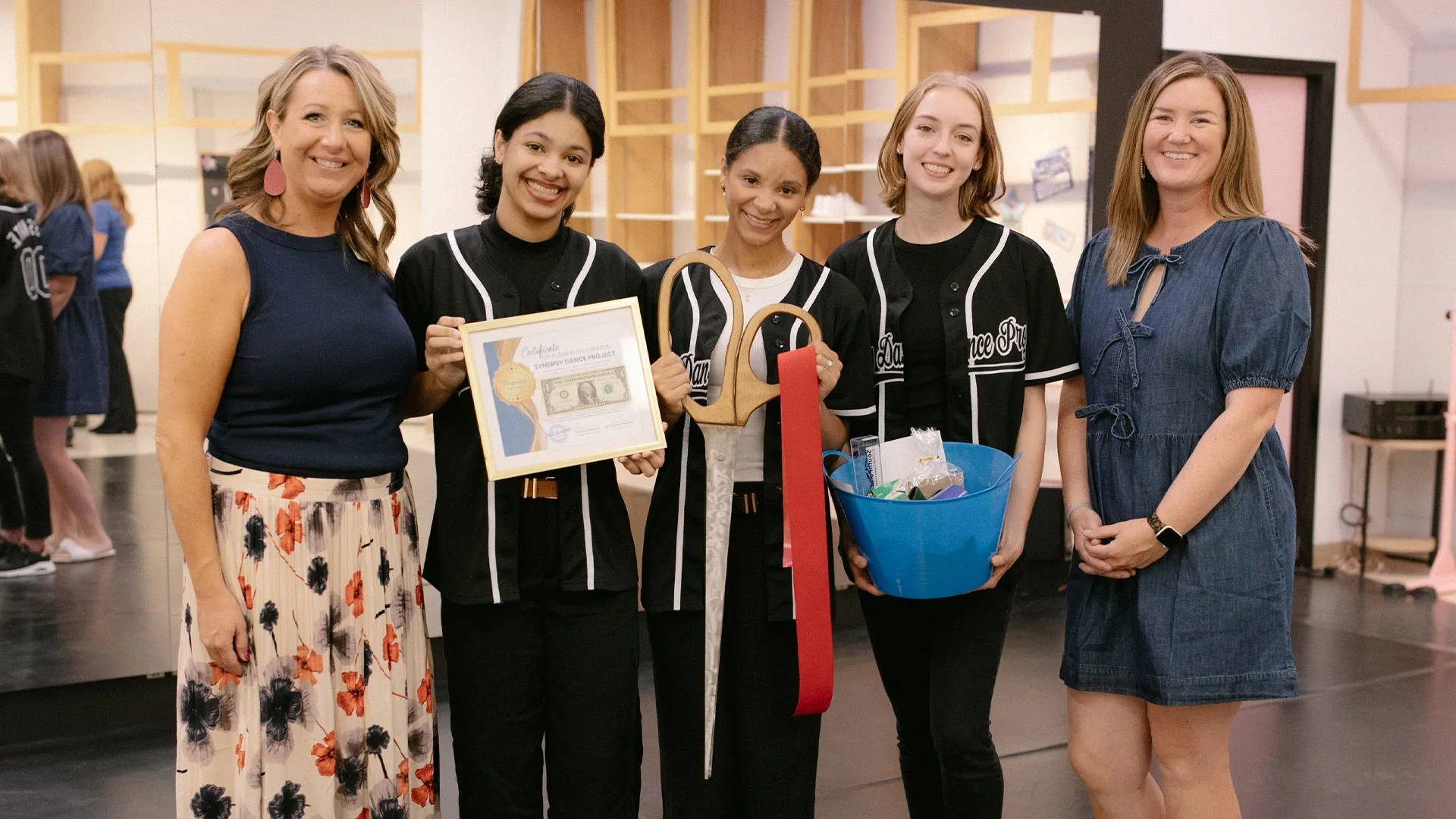 A group of people standing indoors holding an award certificate, a ribbon, and a basket of items.