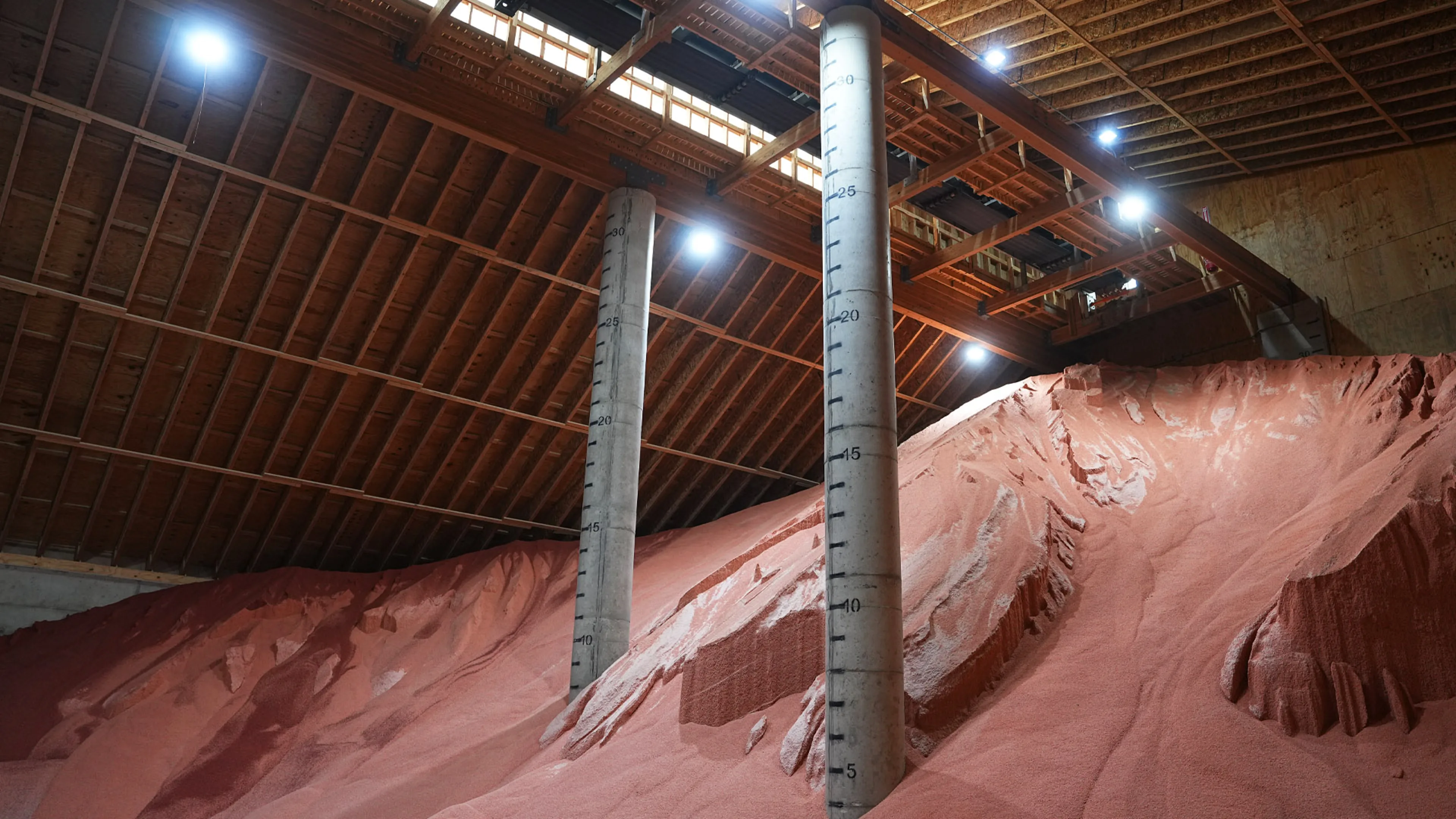 Mounds of grain stacked inside a large storage barn with tall measurement pillars.
