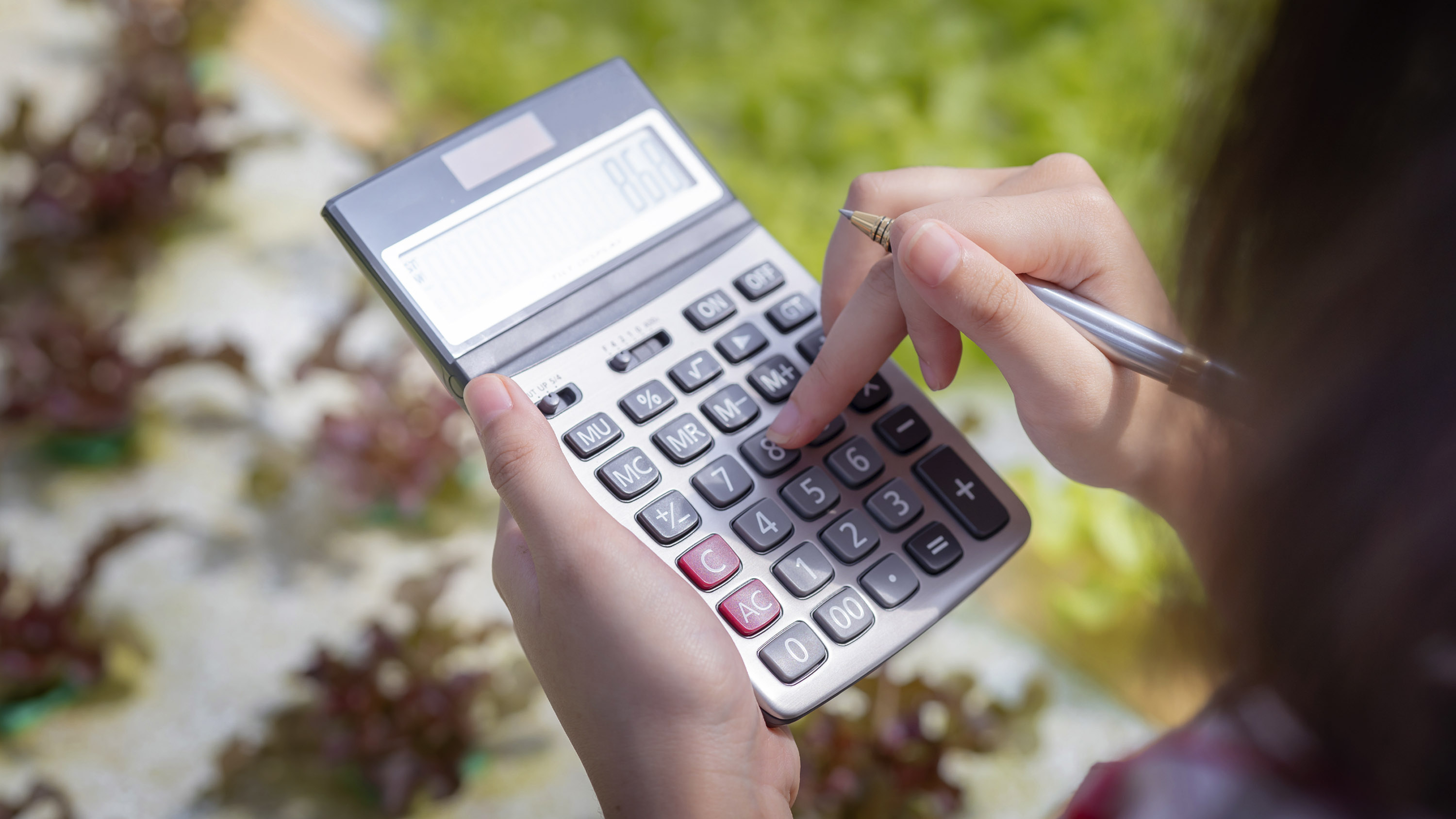 Close up of a female farmer standing over a crop and using a calculator 