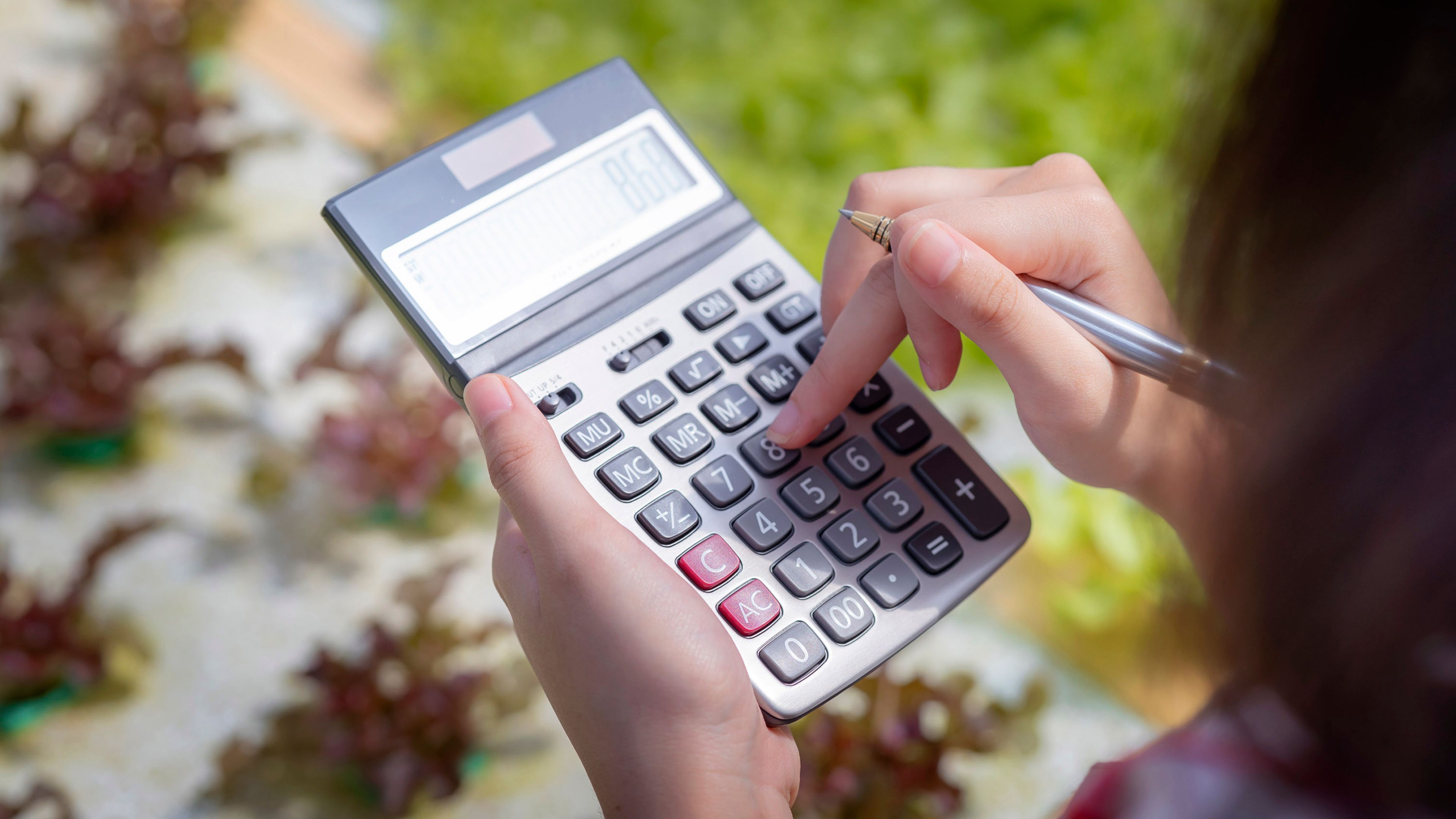 Close up of a female farmer standing over a crop and using a calculator