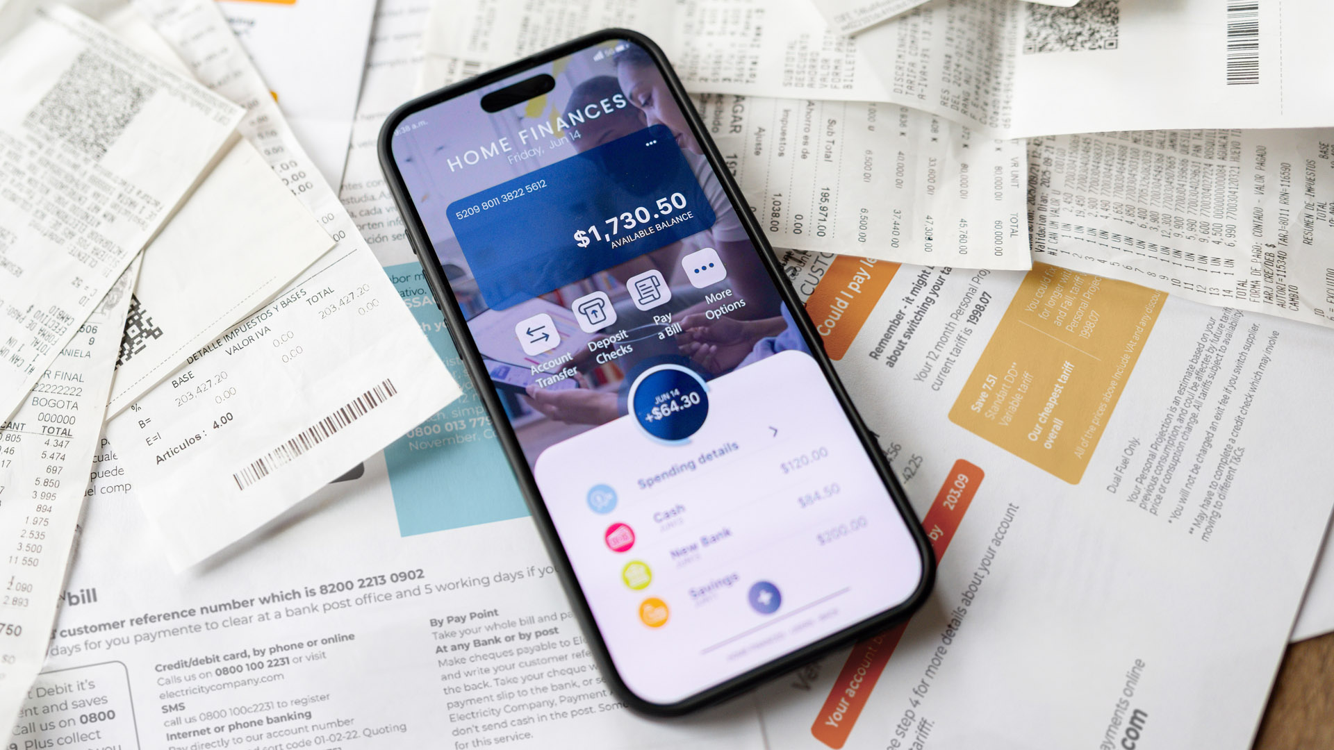 A smartphone displaying a home finance app with a balance of $1,730.50, surrounded by various printed receipts and bills. The app screen features icons for sending money, paying bills, and viewing spending details, with color-coded categories for cash, groceries, and utilities.