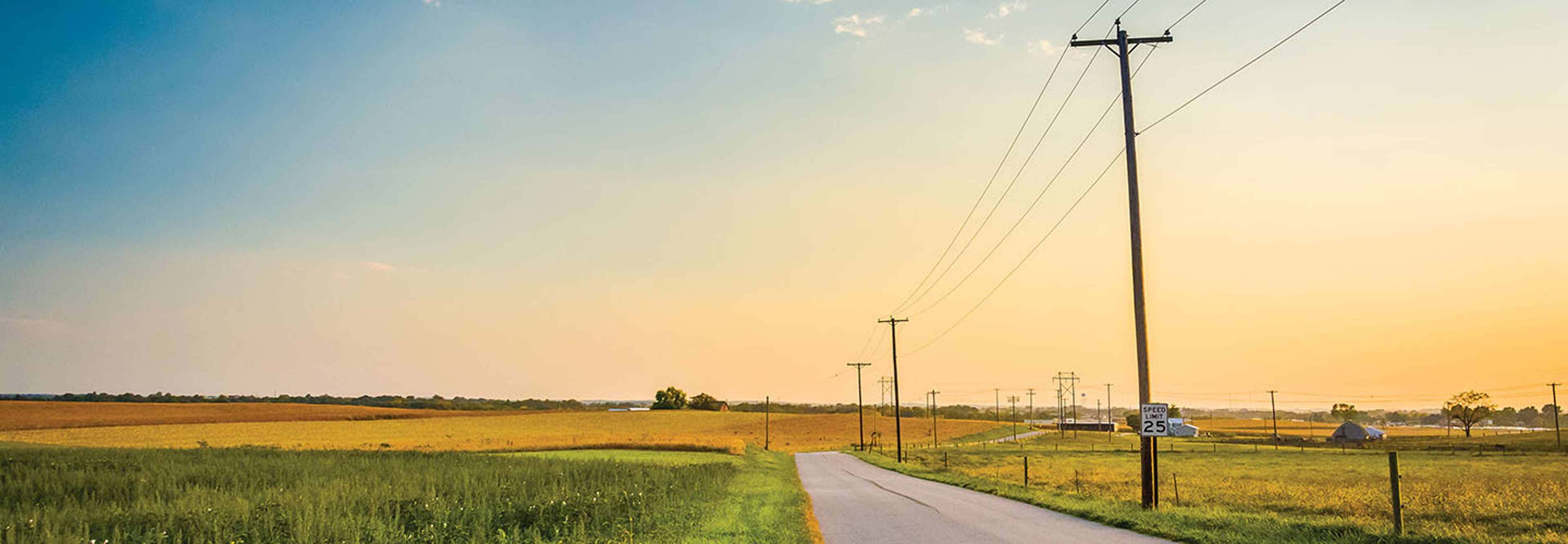 County road with distribution power poles along the side holding cable line surrounded by farmland