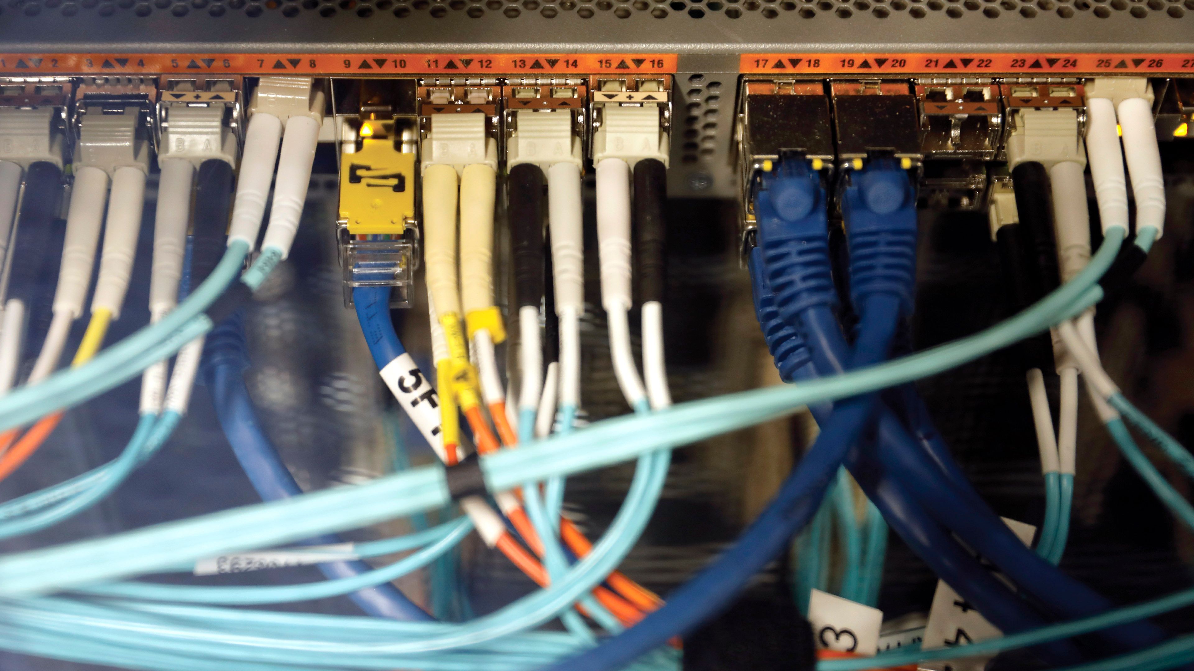 Close view of a network switch or patch panel with multiple Ethernet cables plugged into ports, showing blue, yellow and black cables connected to equipment