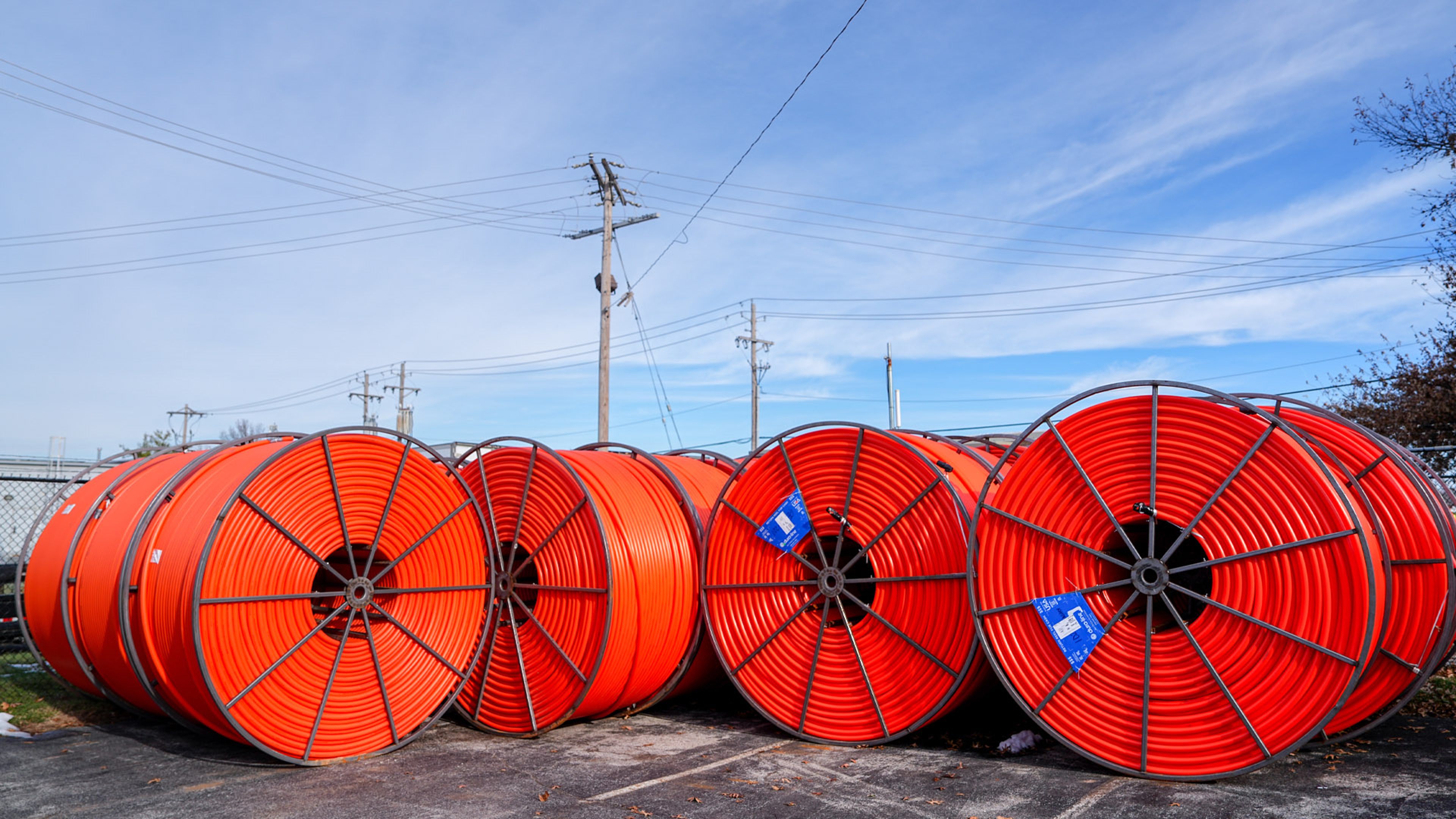 Large orange industrial cable reels lined up outdoors near utility poles.
