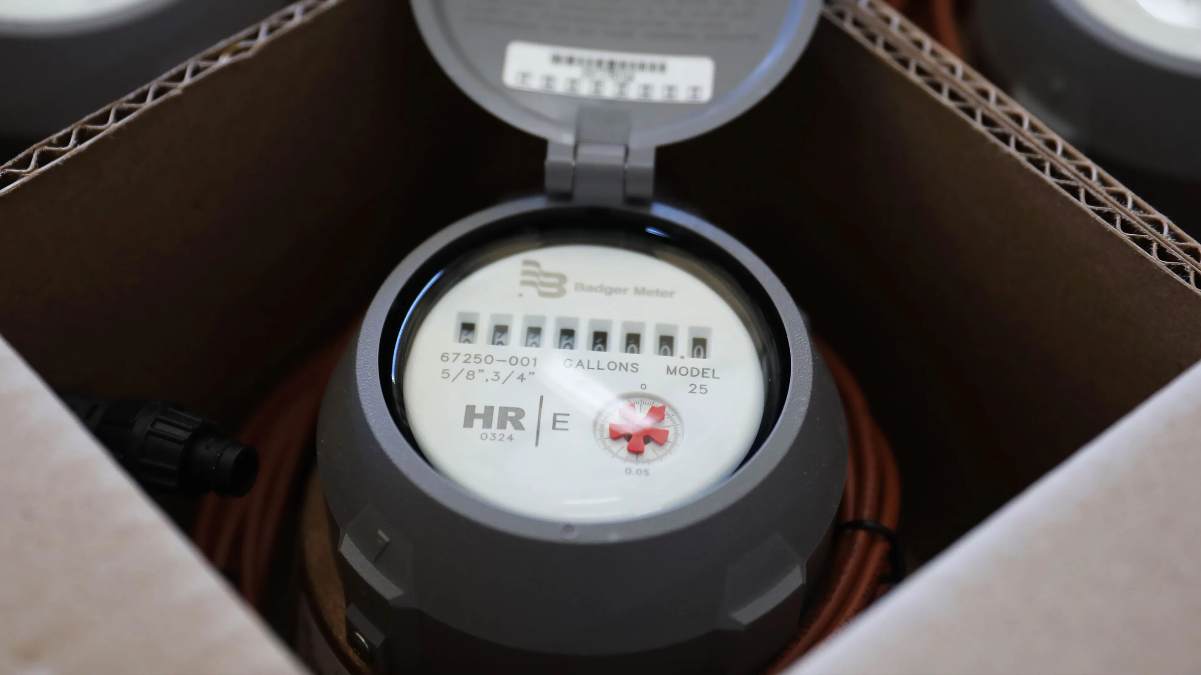 Close view of a water meter device inside a protective enclosure with visible dials and measurement markings