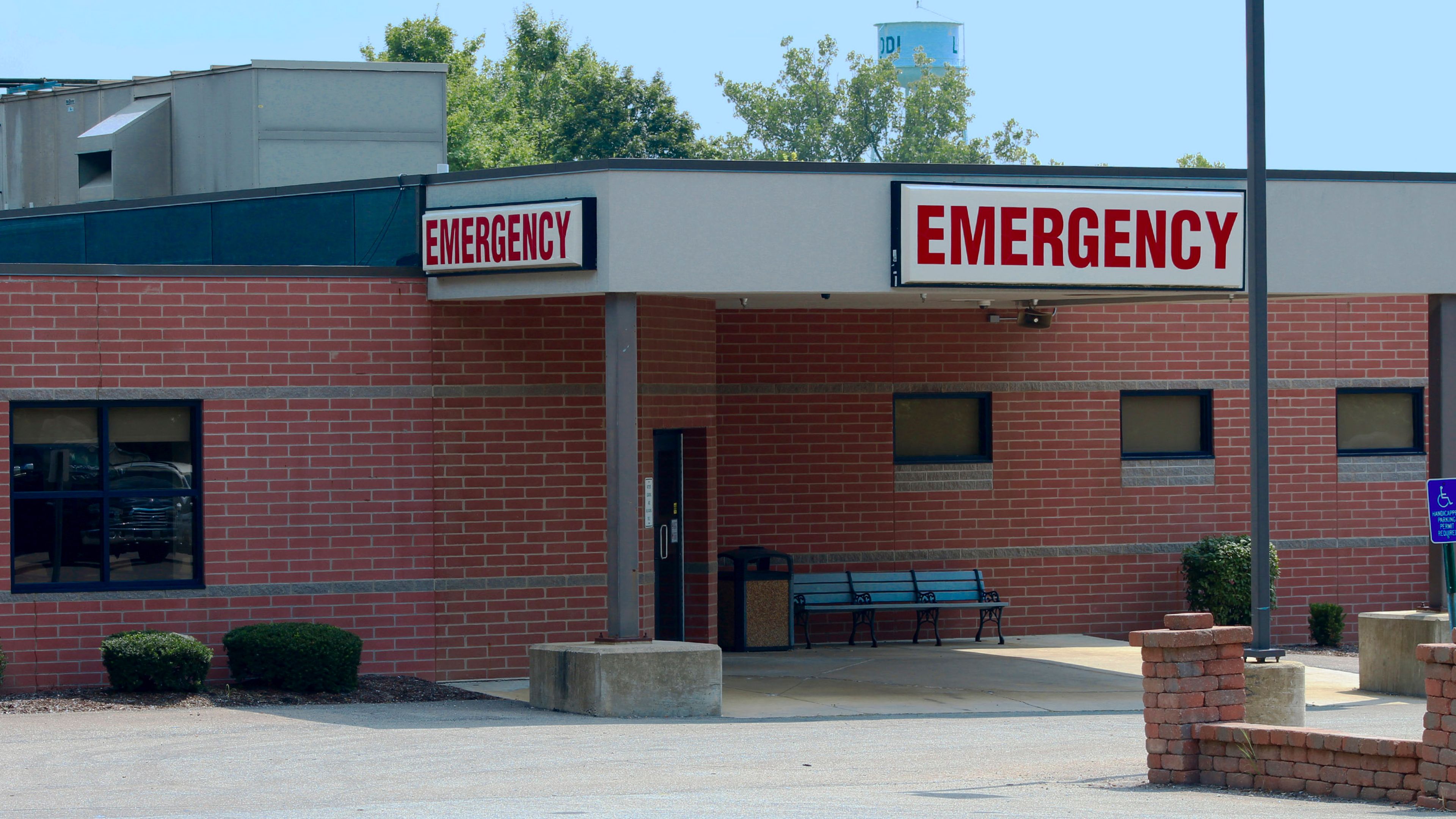 Exterior of a small healthcare facility building with an emergency entrance and signage visible on the structure