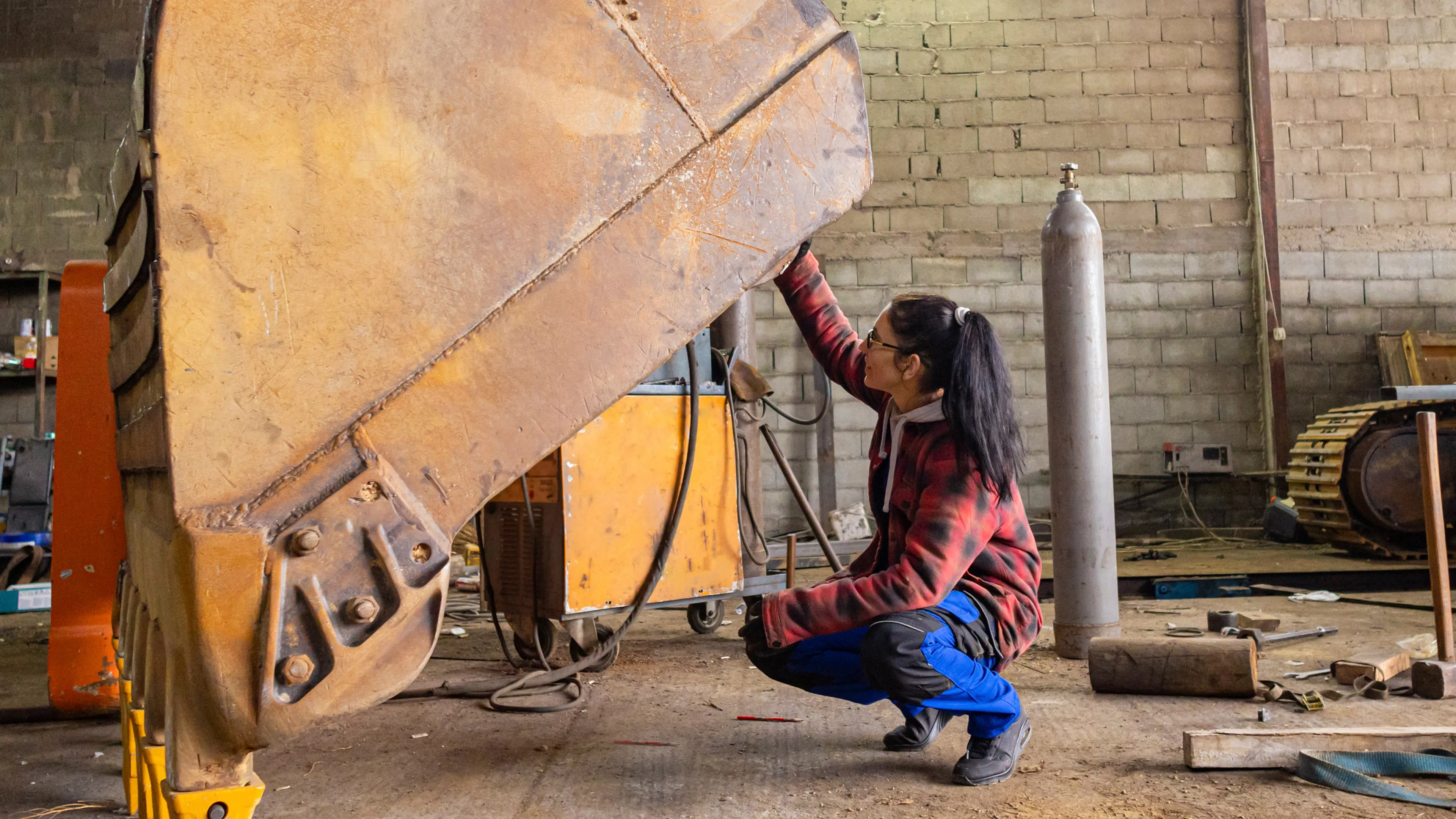 Person working on large industrial equipment inside a workshop with tools, hoses and machinery components visible