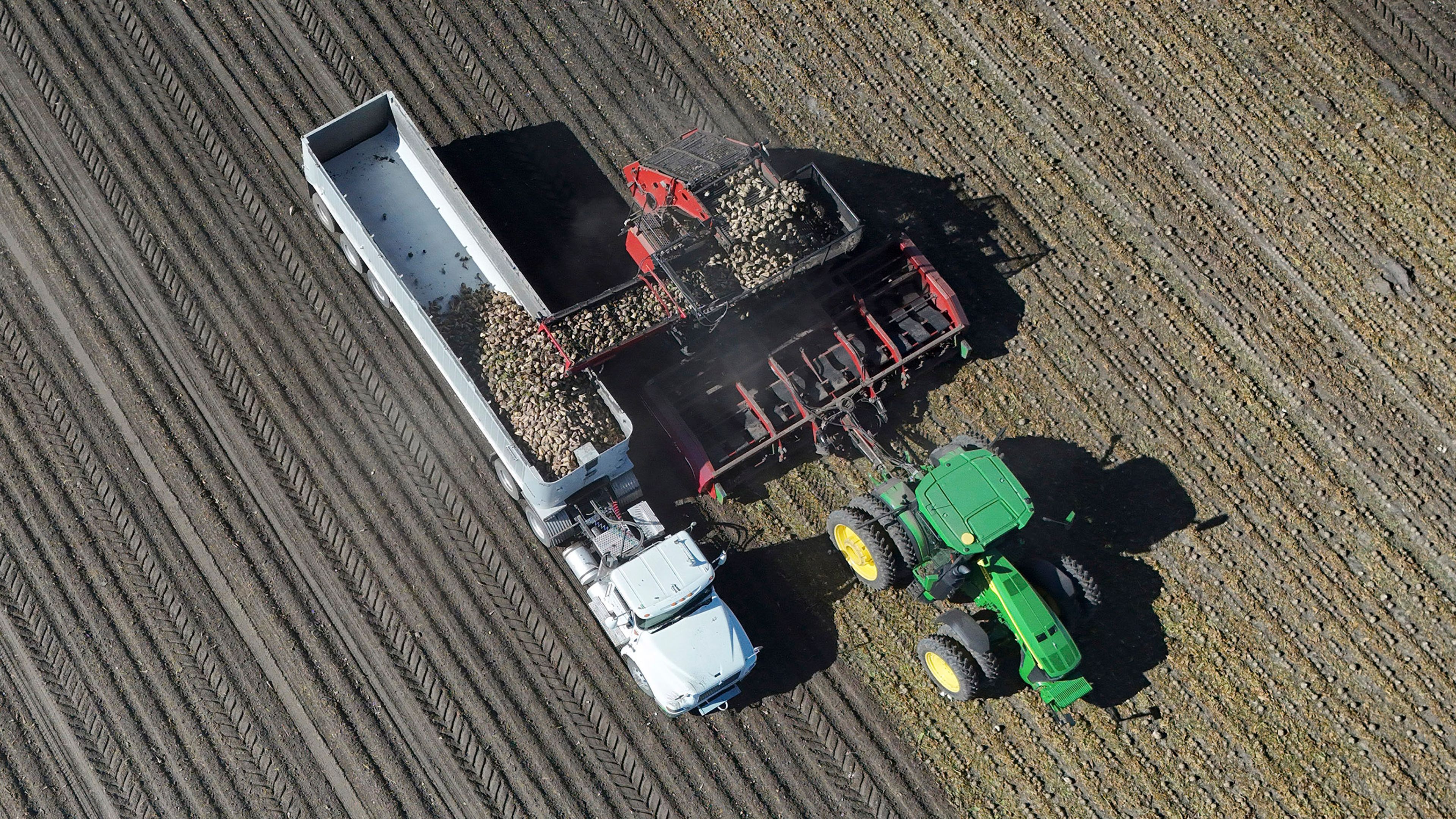 Aerial view of a tractor and harvesting equipment operating in a farm field