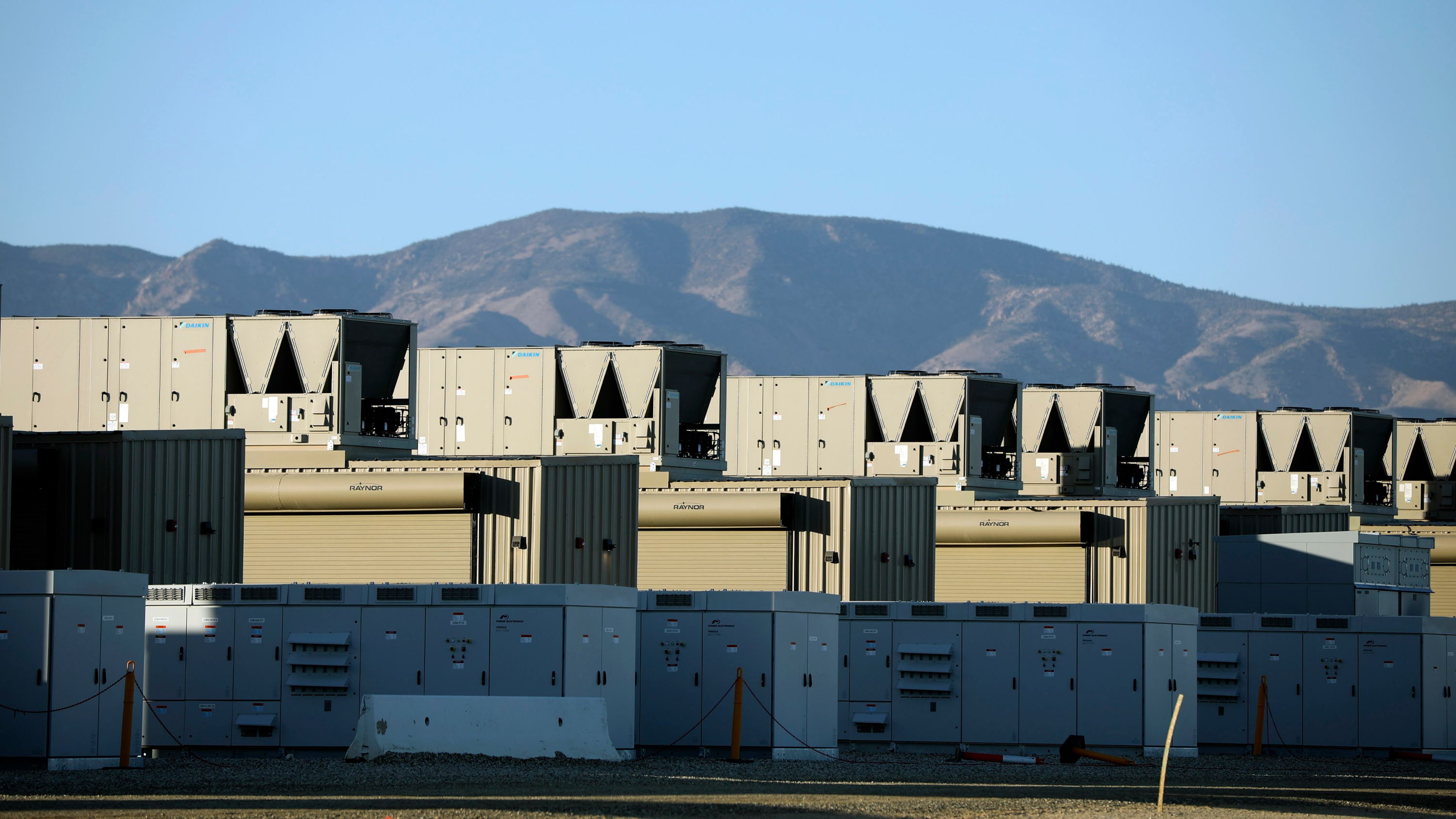 Electrical infrastructure facility with industrial buildings, equipment and transformers set against a landscape with mountains in the distance