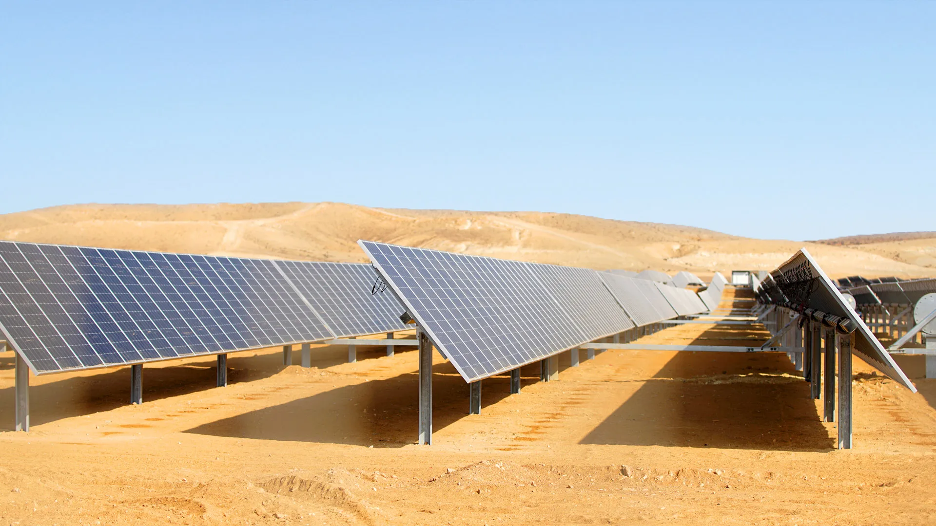 Rows of solar panels installed in a desert landscape under a bright sky.