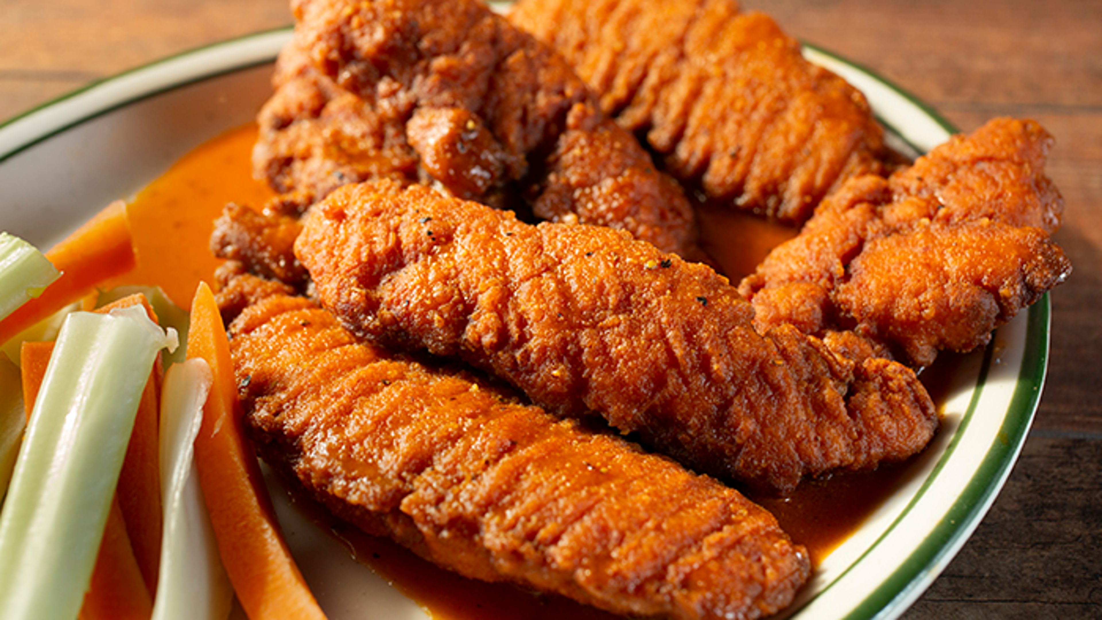 A plate of buffalo chicken tenders served with celery and carrot sticks on the side.