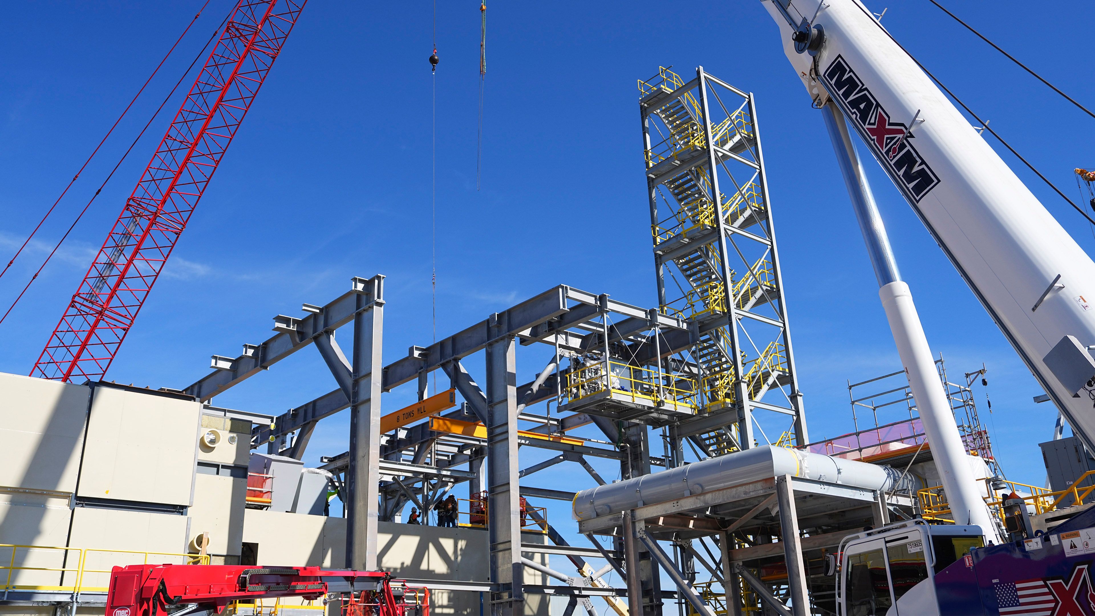 Industrial construction site with large steel framework structures, cranes and workers assembling utility or energy infrastructure