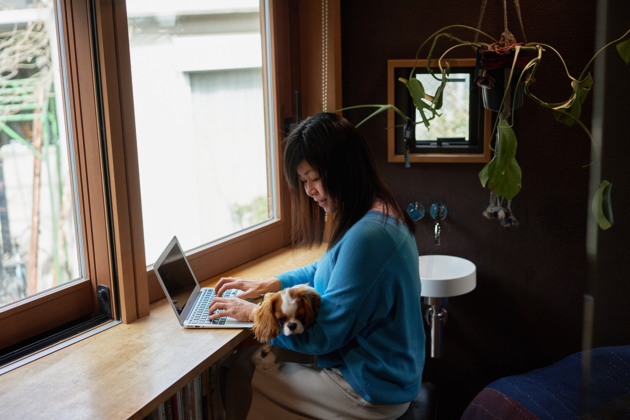 Une personne écrit sur son ordinateur portable, assise à un comptoir près d'une fenêtre.