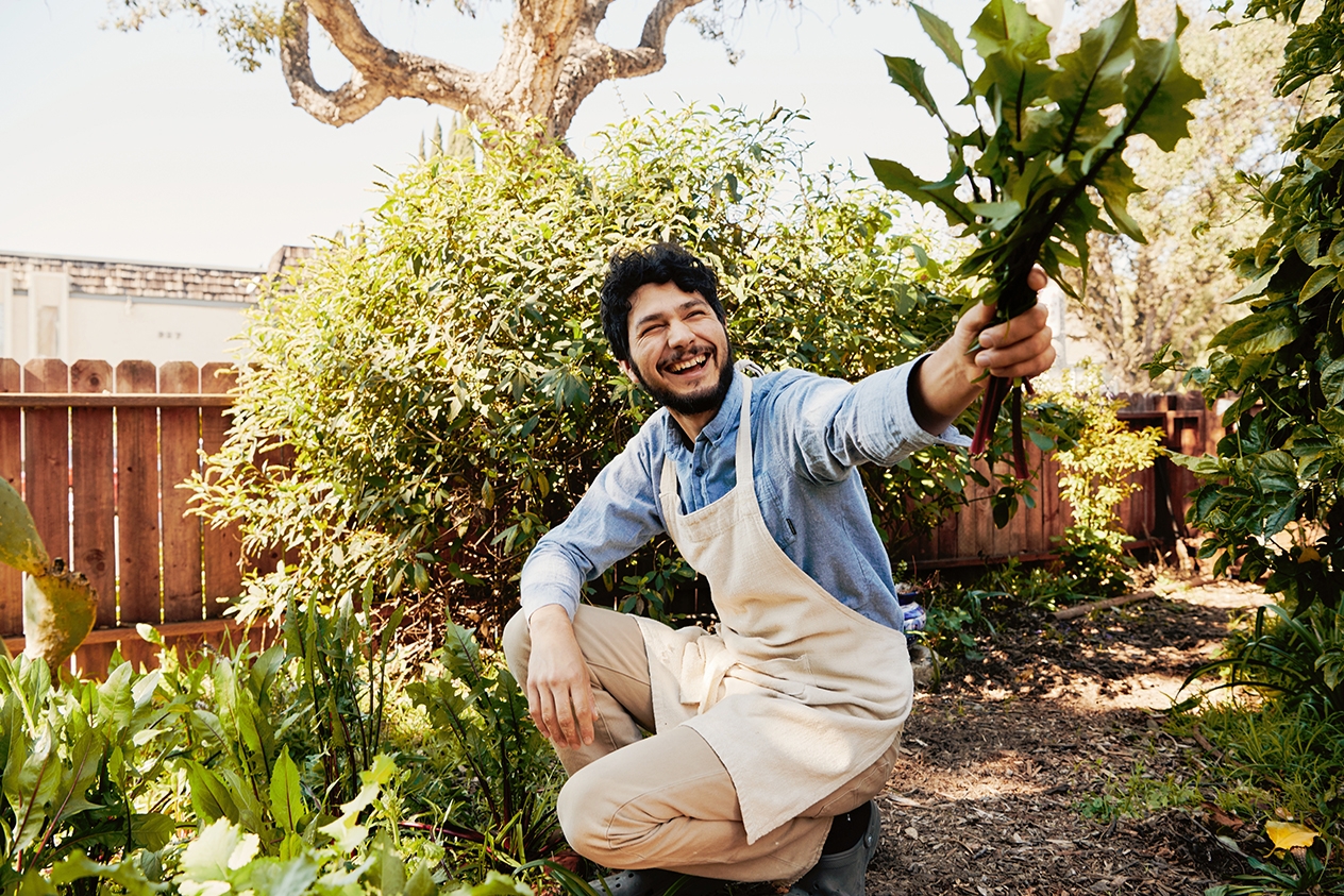 A person working in a garden, holding a bunch of green produce.