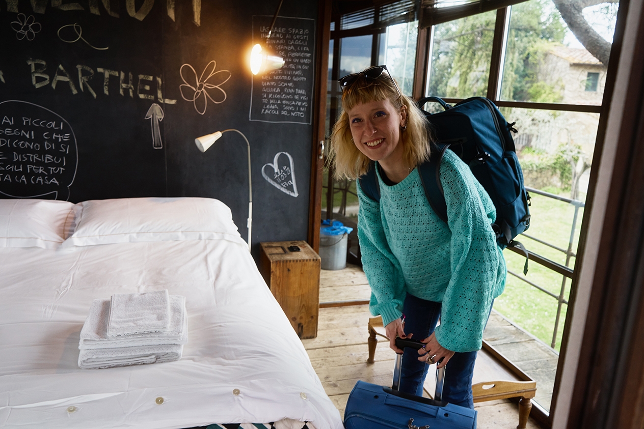 En resenär med resväska och ryggsäck i ett sovrum där hen ska bo.