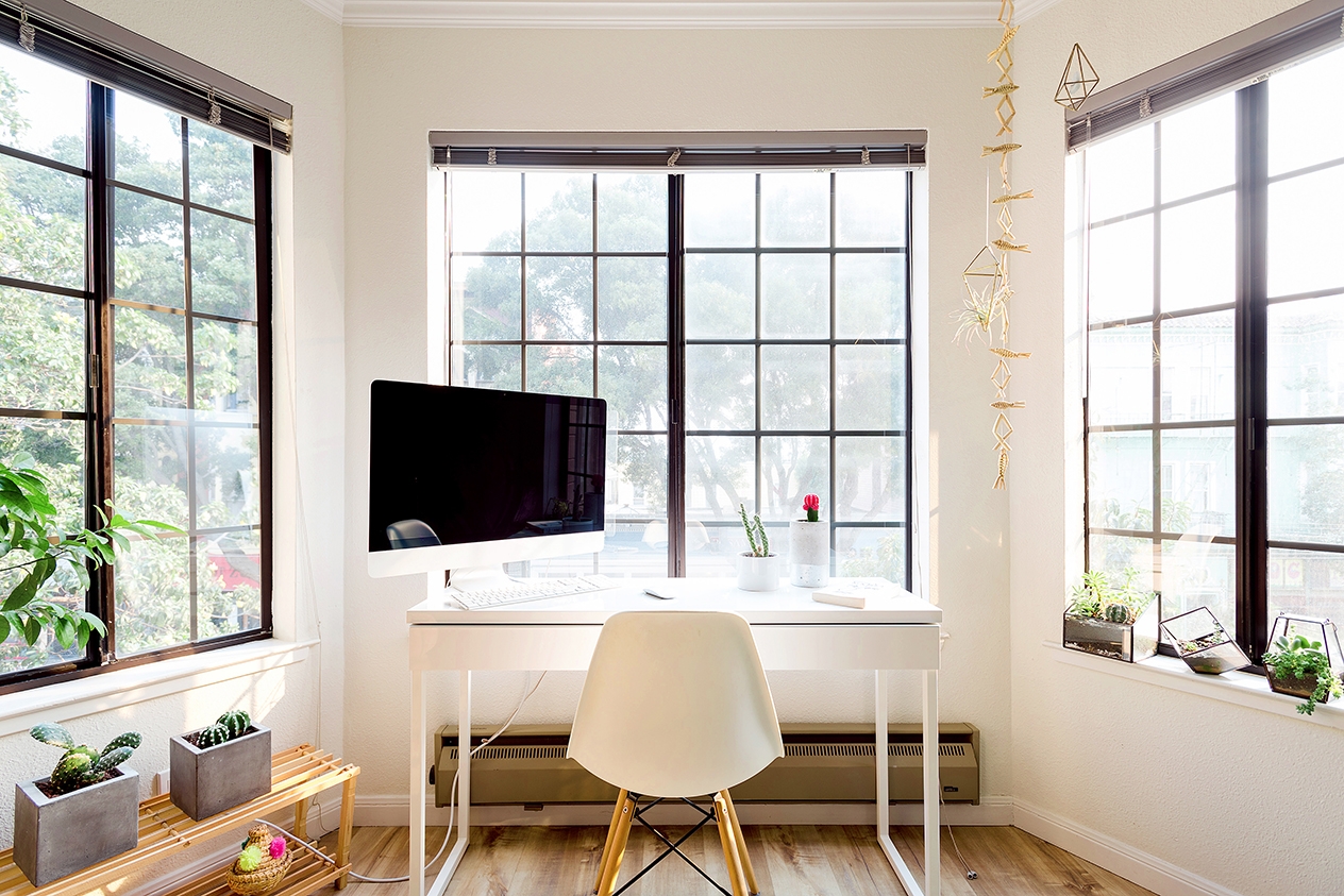 Un escritorio con una silla y un monitor grande en una habitación con tres ventanas.