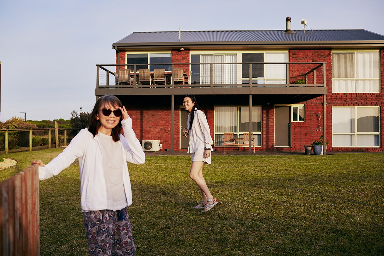 Dos mujeres están en el jardín trasero de una casa de ladrillo rojo de dos plantas con terraza.