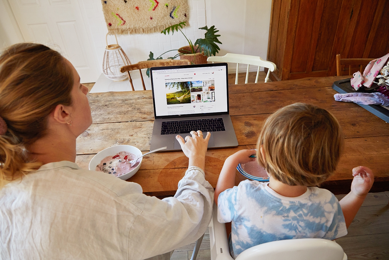 Une femme et un enfant assis à une table, effectuant une recherche de logements Airbnb sur un ordinateur portable.
