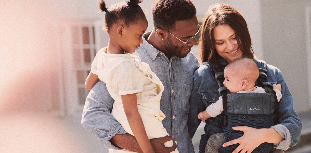 Family on four with a father holding a child and a mother with a newborn in a baby carrier