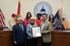 Commissioner Cohen stands with honorees in front of the dais and the other Commissioners stand behind the dais
