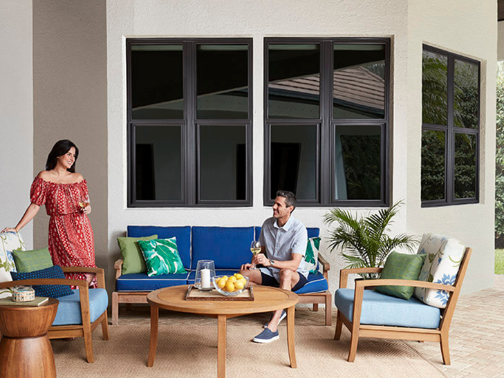 a couple is sitting at a patio with large single-hung windows behind them