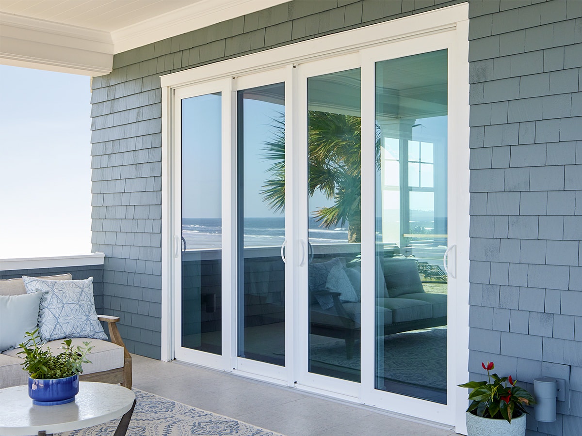 A white four-panel sliding door on a blue-wood-sided home exterior.