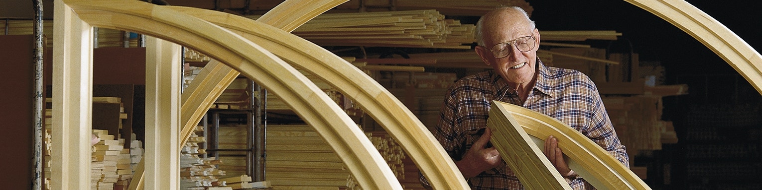 An old man is inspecting the wood on a curved window