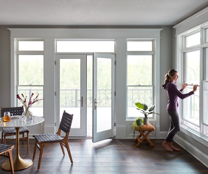 a woman opening a window in a sunroom.