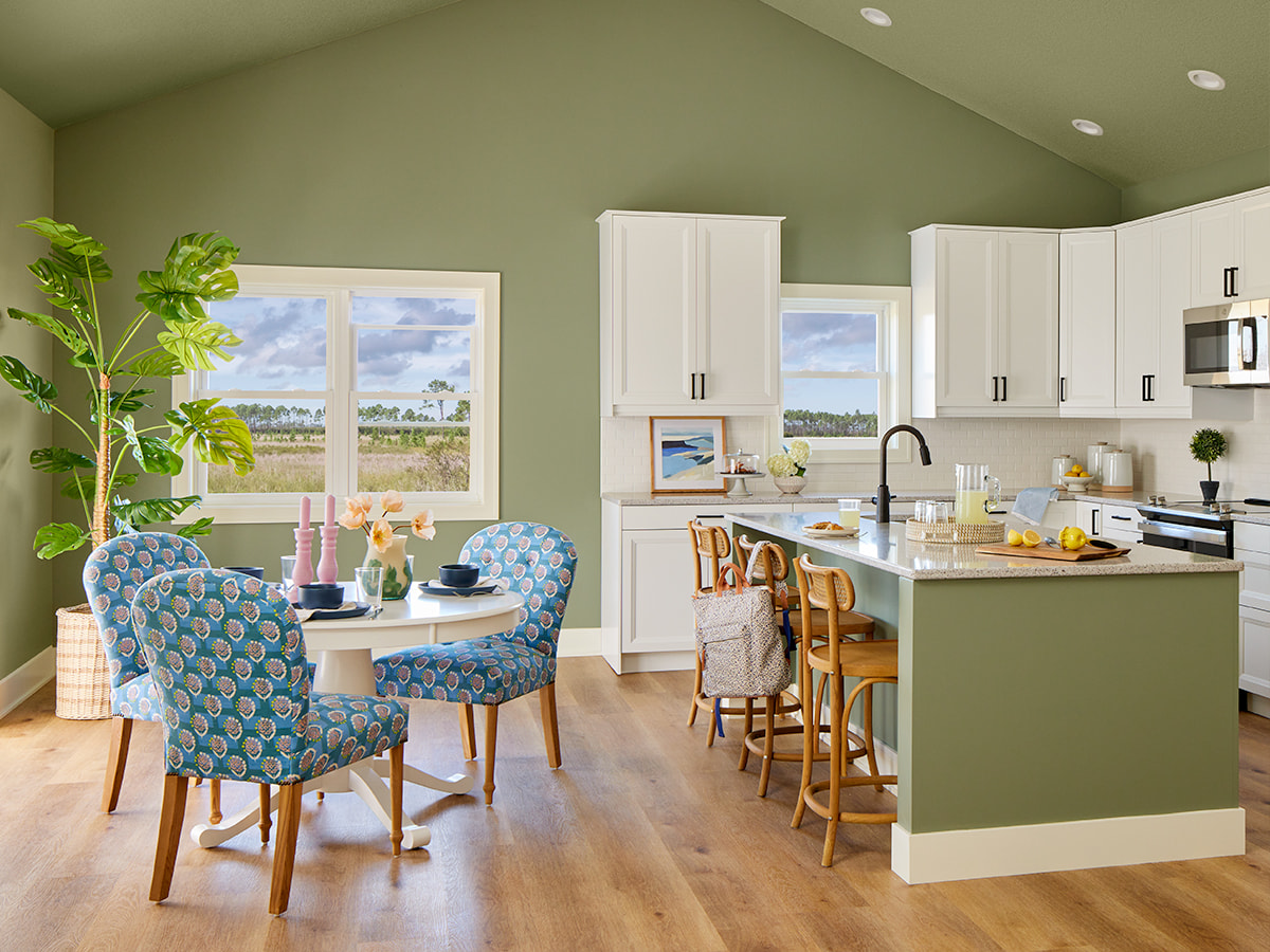 An open-concept kitchen with green walls and white cupboards