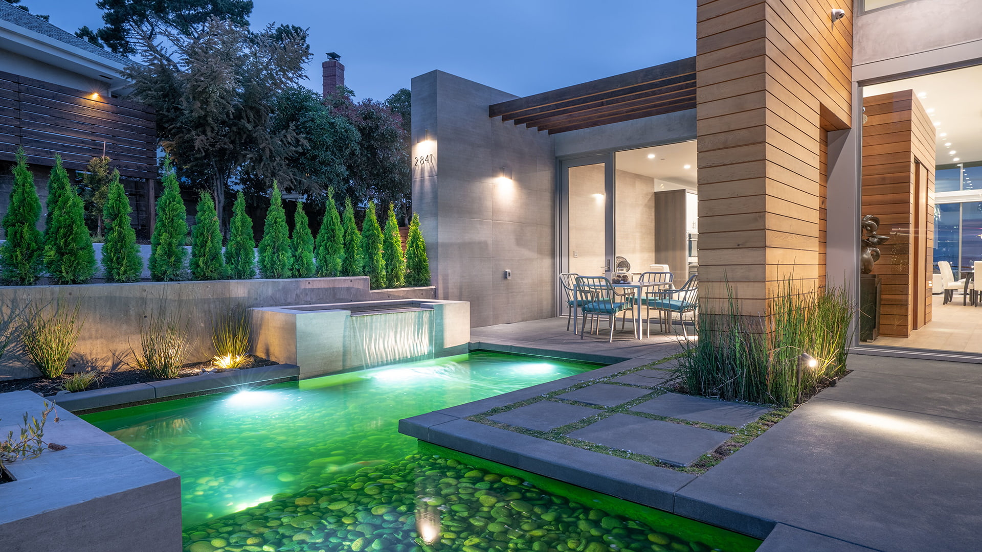 A reflection pool is lit from under the water surrounded by a cement deck