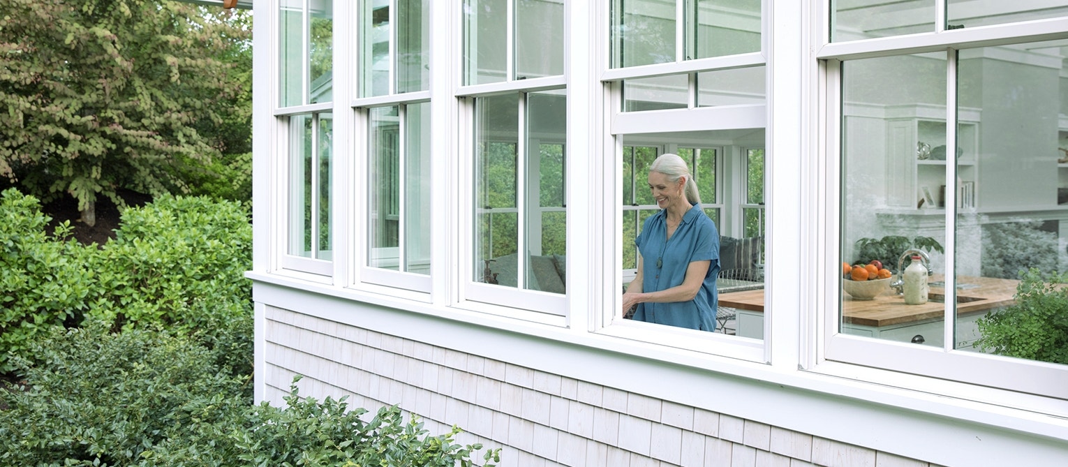 a woman is standing by an open double-hung window