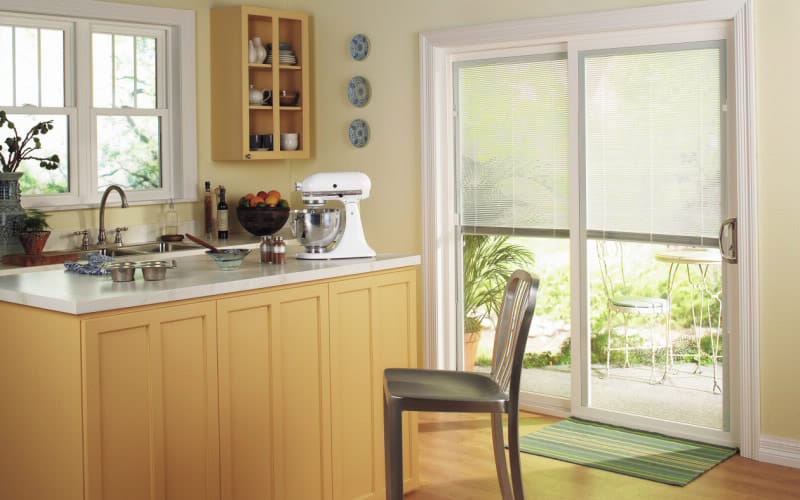 A natural wood and yellow kitchen with a sliding patio door leading to a back patio