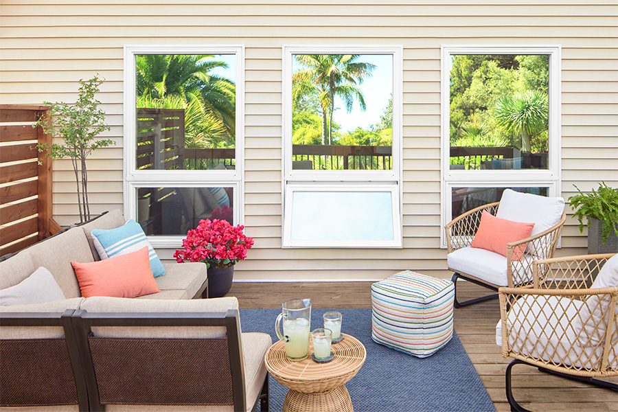 Palm trees are reflecting off three picture windows that have awning windows open below.
