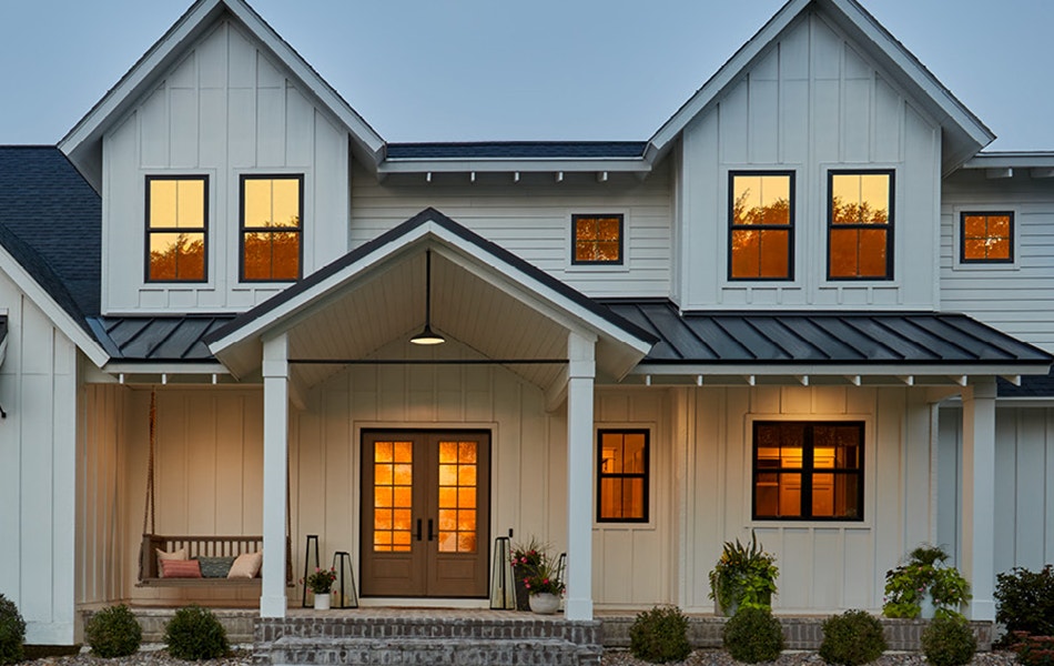 a large white farmhouse whose windows are reflecting the orange sunset