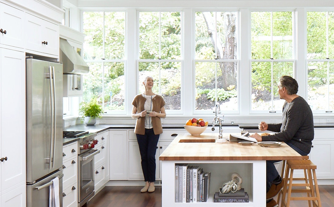 a bright white kitchen with a wall of windows and a big tree outside the windows.