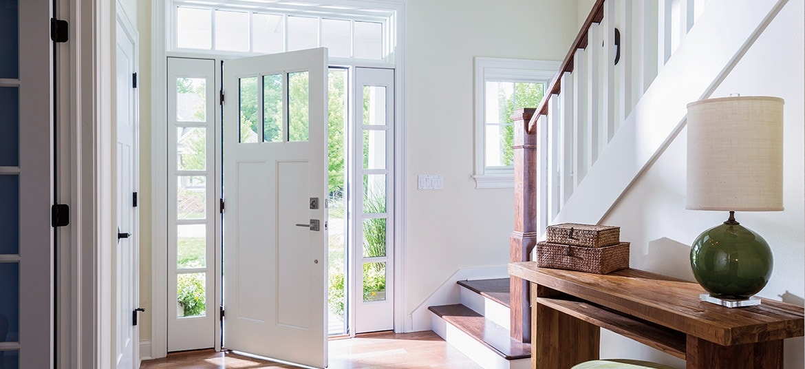A white craftsman entry door opens to a white-painted entryway with wood on the stairs.