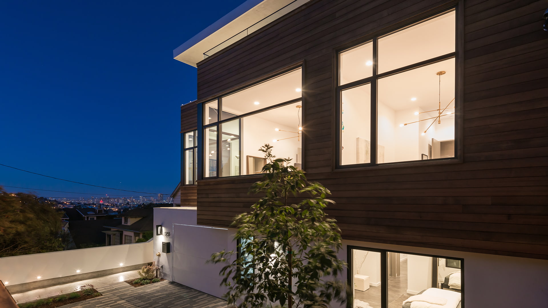 The side of a modern home viewed at night with the city skyline in the distance