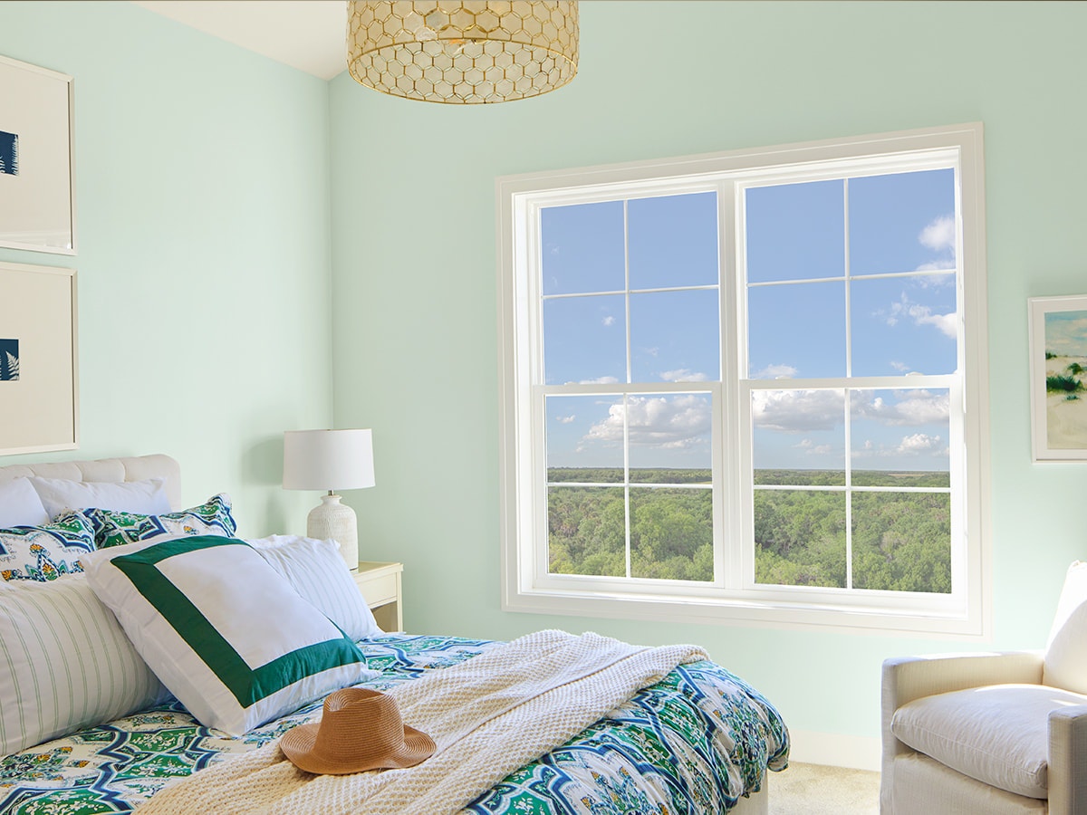 two single-hung windows beside a bed with colorful blue bedding.