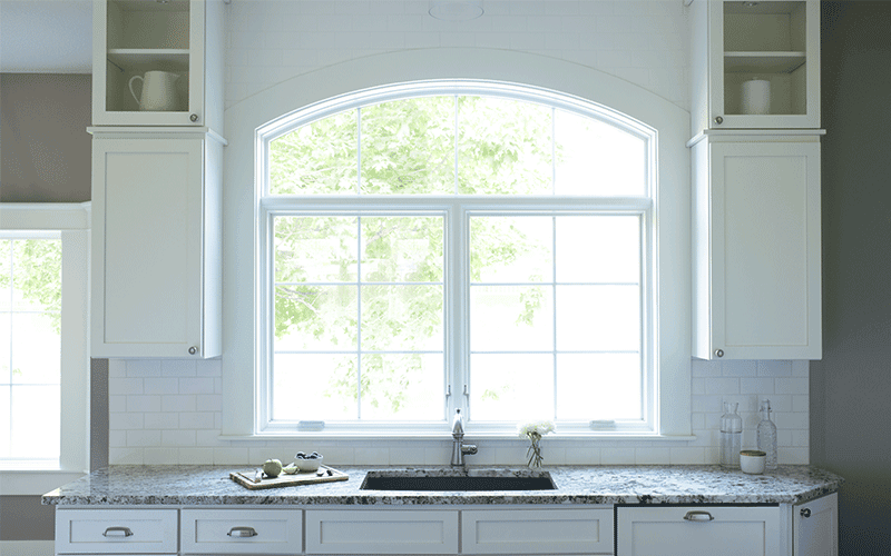 Two white casement windows with an arched transom in a white kitchen