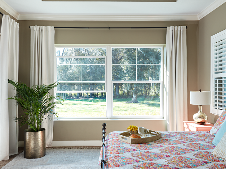 a bedroom with wide double-hung windows between drapery
