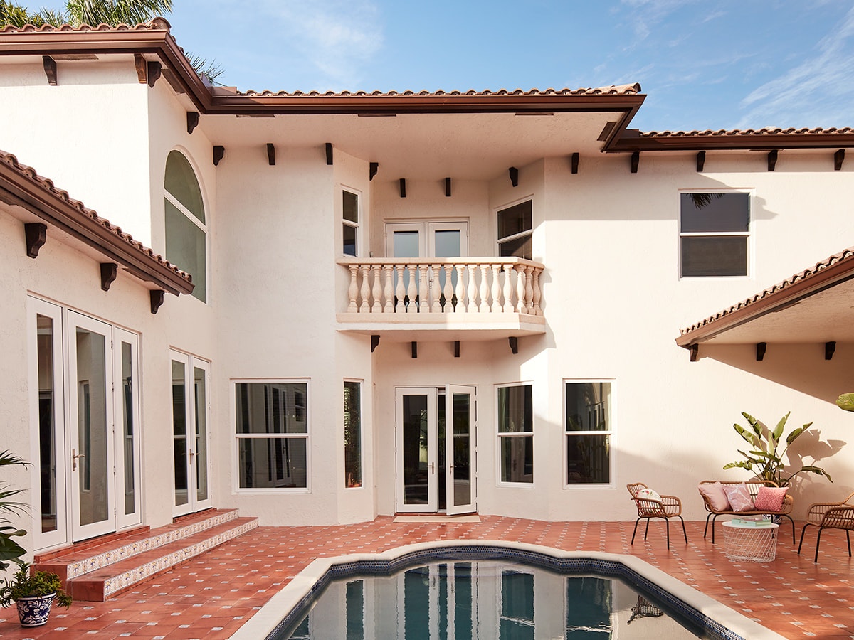 A spanish-style courtyard interior with white french doors on the far side of the pool