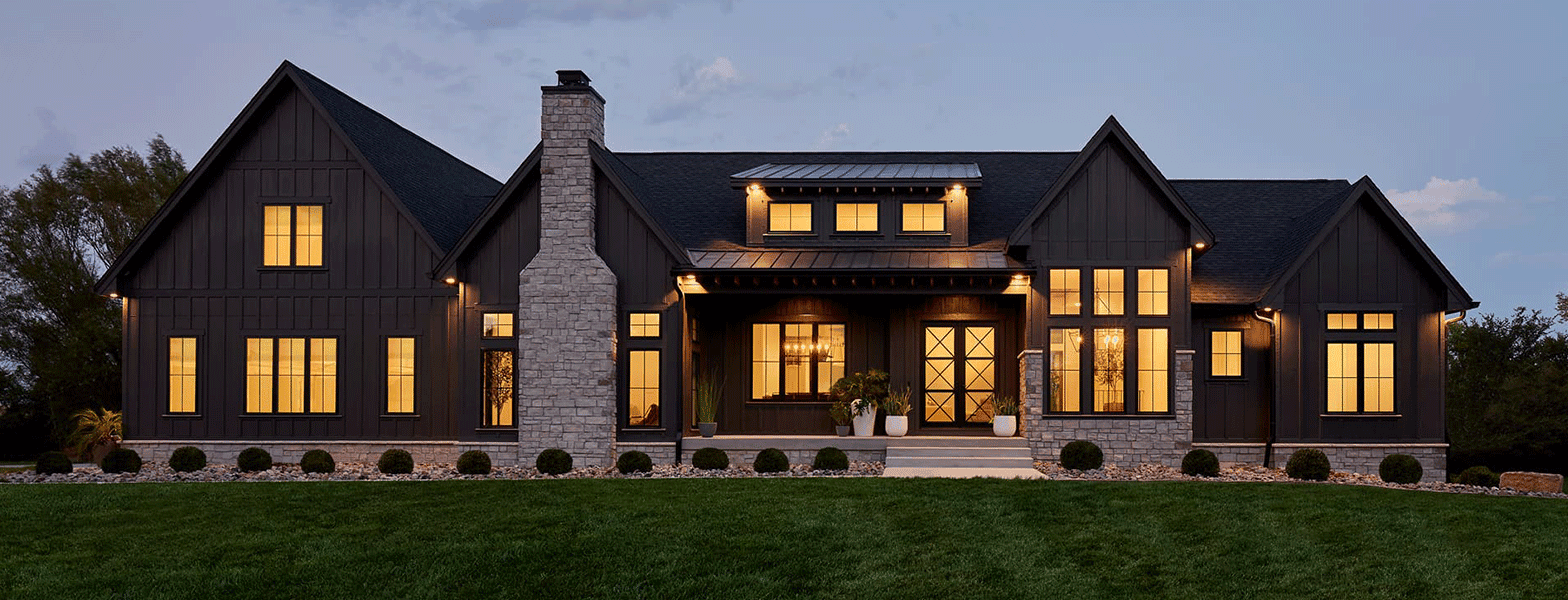 a dark-colored ranch home at dusk with a lot of light coming out of the many windows.