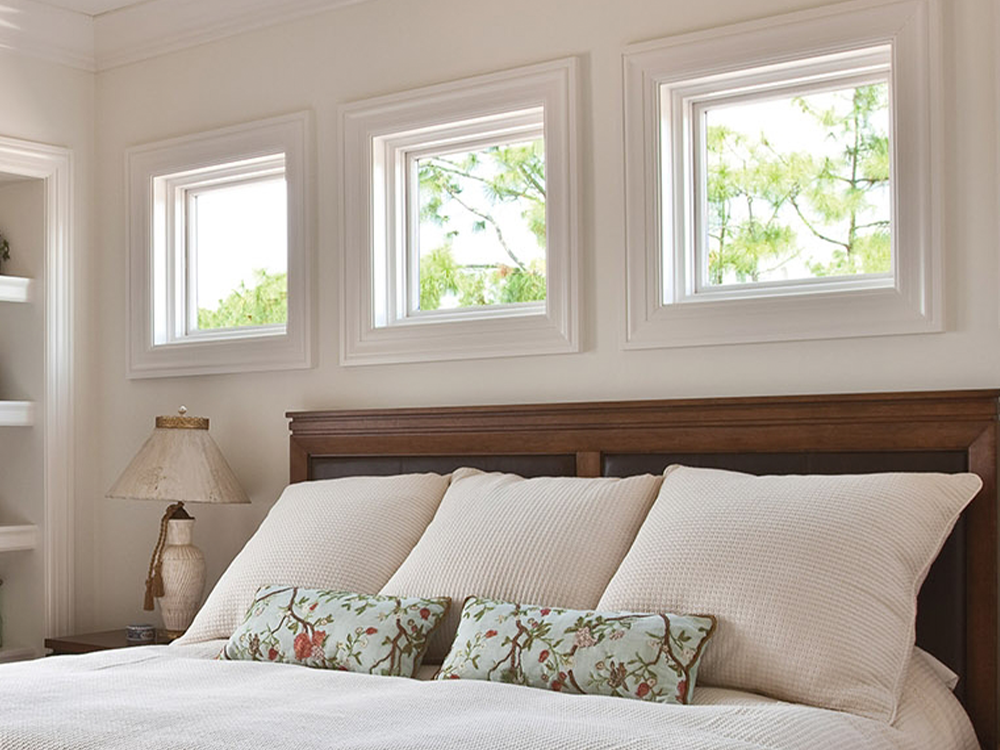 three awning windows over a bed with cream-colored sheets and pillows