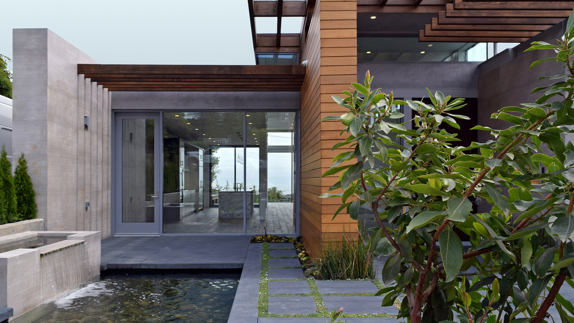 Cement patio with natural grass between the cement tiles in front of a hinged door with a window wall aside