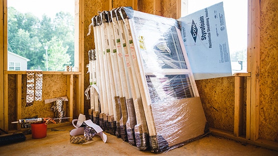 a group of new Pella windows wrapped in plastic and waiting to be installed