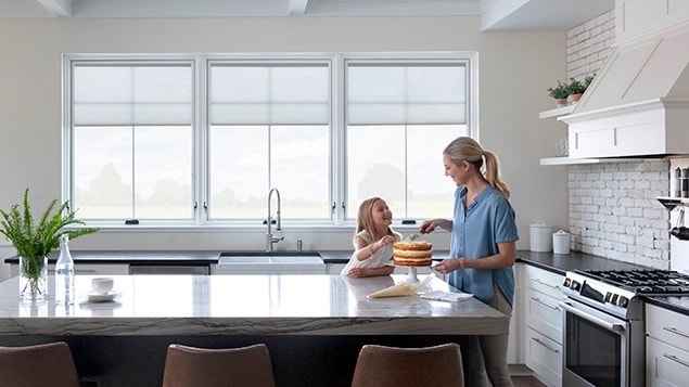 a mom and daughter frosting a cake in front of large casement windows