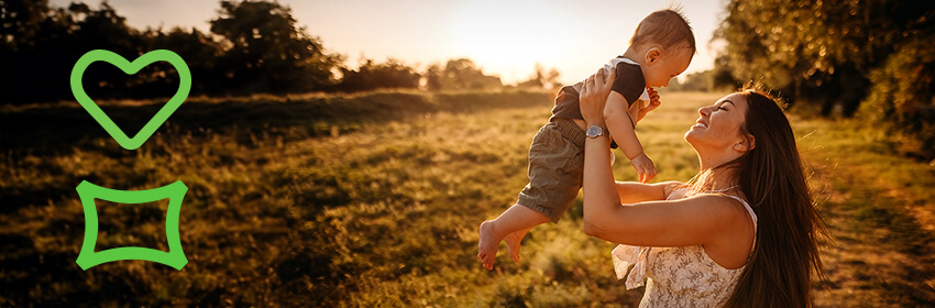 Smiling mother lifting baby above her head in a field at sunset
