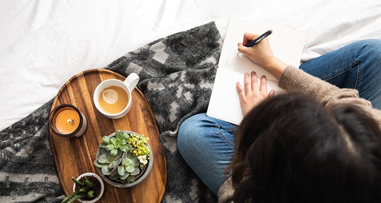 Woman writing next to a tray with coffee, candle and potted succulents 2 