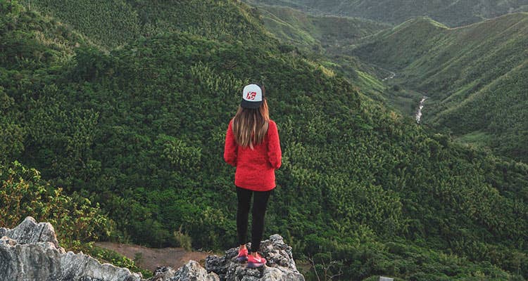 Girl wearing an XS cap standing at the edge of a mountain top 